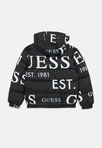 Doudoune noire avec le texte blanc "GUESS" et de grands chiffres, dotée d'une capuche et de poignets élastiques, fabriquée en nylon lisse et brillant.