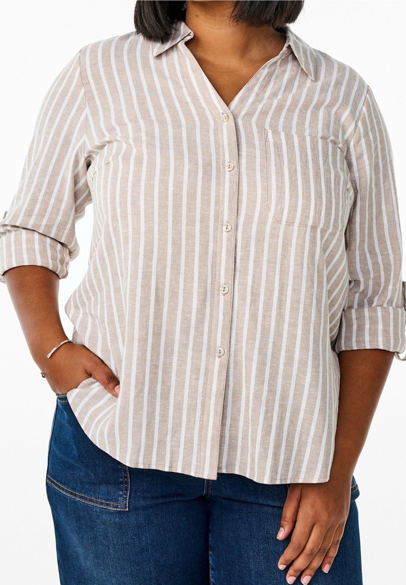 Camicia button-up beige chiaro con strisce bianche verticali, colletto e una singola tasca sul petto. Il tessuto sembra essere strutturato.