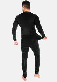 Schwarzer sportlicher Thermoanzug aus dehnbarem Stoff mit langen Ärmeln und Hosen, akzentuiert mit grünen Linien und einer figurbetonten Passform.