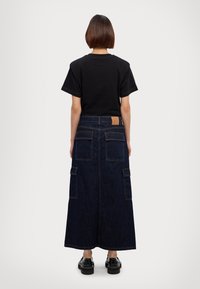 Zwarte t-shirt met korte mouwen, gecombineerd met een lange donkere spijkerrok met klepzakken en een leren merketiket op de taille.