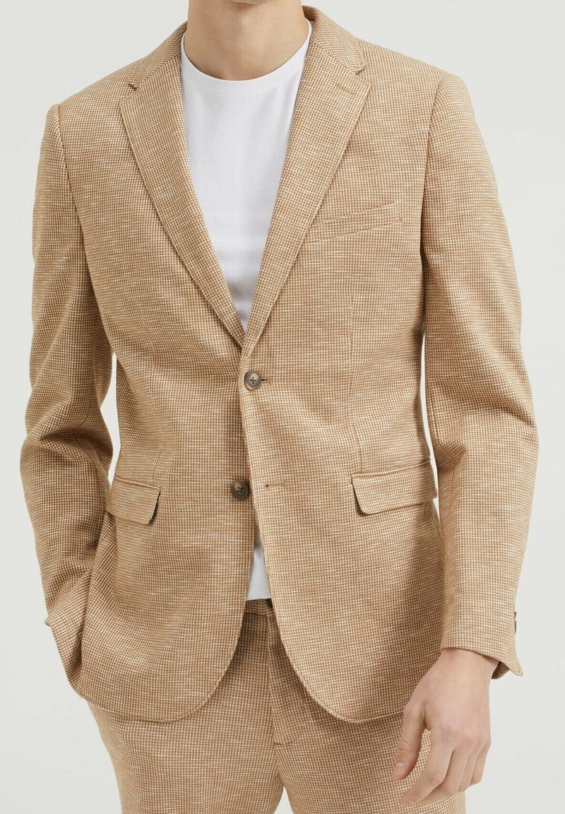 Brun rutig kavaj i texturerad tyg med en knapp, slagkrage och två sidofickor, tillsammans med en vit t-shirt.