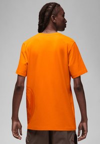T-shirt di cotone arancione con maniche corte, silhouette leggermente oversize e un dettaglio grafico testurizzato sul lato inferiore.