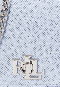 Materiale testurizzato azzurro chiaro con una catena argentata e un logo metallico con il dettaglio "RL" in evidenza.