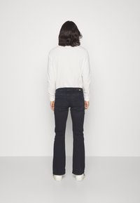 Jeans acampanados de color azul oscuro con una textura suave, con un diseño en el bolsillo trasero. Combinados con una camiseta blanca de manga larga lisa.