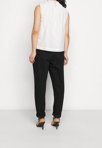 Vit texturerad ärmlös topp med en nyckelhålsrygg, ihop med lösa svarta byxor och klacksandaler. Enkel och ren design.