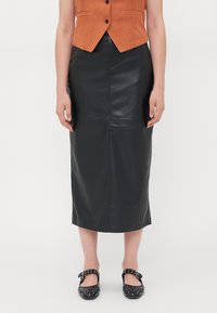 Zwarte leren midi-rok met een aansluitende silhouet, gladde textuur, verticale naden en een minimalistisch ontwerp. Gepaard met zwarte studschoenen.