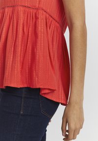 Rød peplum top med strukturerede striber, der har en tætsiddende krop og flærret kant, parret med mørkeblå denim jeans.
