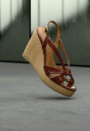 Brown patent leather wedge sandal with woven rattan platform and ankle strap, displayed against a muted green and gray background.
