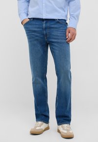 Jasnoniebieskie dżinsy o prostym kroju, z pięcioma kieszeniami i subtelnym wyblaknięciem. Połączone z neutralnymi trampkami.