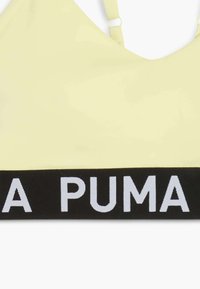 Sujetador deportivo amarillo hecho de una tela suave con un diseño de escote en V profundo y tirantes ajustables. Presenta una banda negra con "PUMA" en texto blanco.