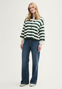 Grün-weiße gestreifte Strickjacke mit Knopfverschluss, kombiniert mit blauen weiten Jeans aus einem glatten Stoff und lockerem Schnitt.