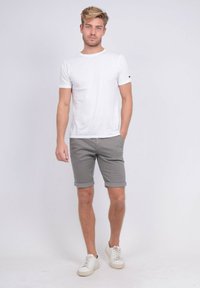 T-shirt blanche à manches courtes associée à un short gris retroussé, complété par des baskets blanches. Design simple et décontracté avec un tissu léger.