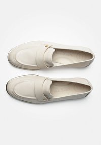 Beige leren loafers met een ronde neus, voorzien van een gestikte ontwerp, metalen accenten en een zachte binnenzool met het label 'SUPER SOFT.'