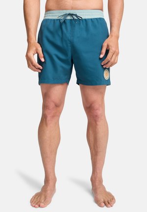 Zielone kąpielówki z elastycznym pasem i sznurkiem do wiązania, z okrągłą naszywką z logo po jednej stronie. Gładka faktura, długość do powyżej kolan.