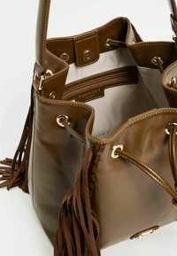 Borsa a secchiello in finta pelle marrone con hardware dorato, tasca interna con zip, chiusura a coulisse e lunghi dettagli a frangia.