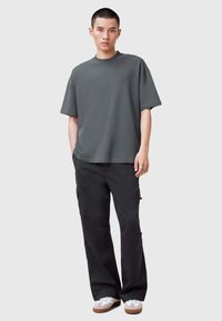 Grå bomullströja med rundad halsringning, avslappnad passform. Matchad med svarta cargobyxor med sidofickor och vita sneakers med bruna sulor.