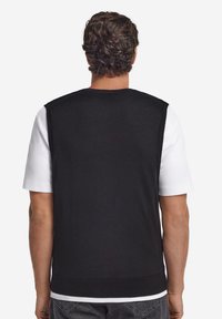 Schwarzer ärmelloser Pullover über einem weißen Hemd, mit Rundhalsausschnitt und glatter Textur, mit geripptem Saum und sichtbaren Schulternähten.