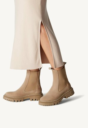 Braune Chelsea-Boots mit elastischen Seiteneinsätzen, strukturierter Wildleder-Oberfläche und klobigen Gummisohlen. Getragen mit einem gerippten, gespaltenen Rock.