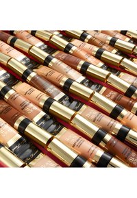 Des rangées de flacons de fond de teint avec des bouchons dorés. L'emballage présente des nuances allant du beige clair au beige foncé, étiqueté "Born This Way Soft Matte Foundation."
