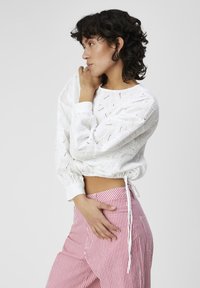 Haut court en eyelet blanc avec des manches longues et un cordon de serrage à la taille, associé à un pantalon rayé rose et blanc taille haute.