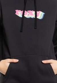 Sweat à capuche noir avec un logo "ROXY" multicolore. Il possède une poche avant et des cordons de serrage, avec un tissu doux et texturé.