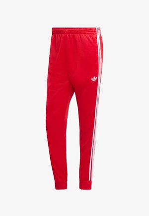 Červené športové nohavice z hladkej látky, s bielymi bočnými pruhmi a vyšívaným logom na ľavej stehne. Elastický pás.