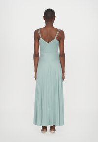 Une longue robe plissée de couleur vert menthe clair avec de fines bretelles réglables et une fermeture à ouverture en forme de clé au dos. Tissu lisse avec une silhouette fluide.