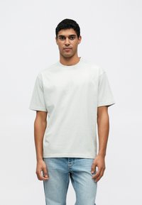 Ανοιχτό γκρι βαμβακερό t-shirt με στρογγυλή λαιμόκοψη, κοντά μανίκια και άνετη εφαρμογή, συνδυασμένο με μπλε τζιν παντελόνι με ίσια πόδια.