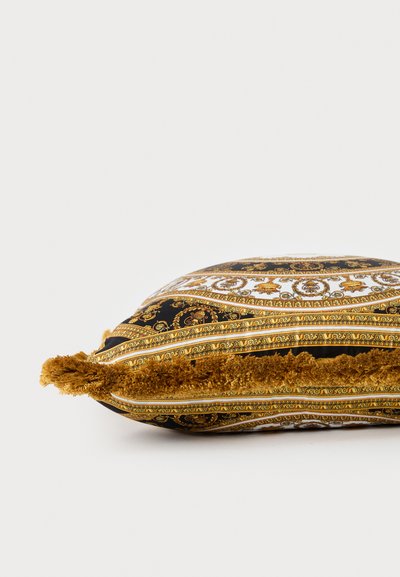 Διακοσμητικό τετράγωνο μαξιλάρι με χρυσά και μαύρα περίτεχνα μοτίβα και καφέ φούντες στις άκρες σε λευκό φόντο.