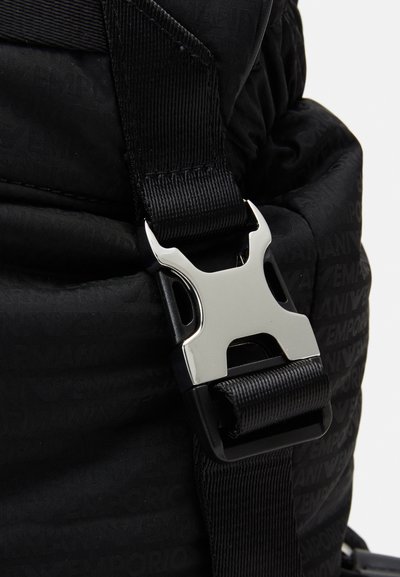 Zaino in nylon nero con texture trapuntata, dotato di una fibbia in metallo argentato e cinghia in tessuto nera. Logo in rilievo discreto visibile.