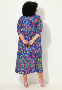 Vestido morado de longitud media con estampado floral y mangas tres cuartos. Presenta puntos coloridos en azul, verde, naranja y rojo.
