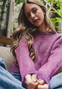 Gebreide trui in verschillende paarse tinten met een ribbeltextuur. Lange mouwen en een ontspannen pasvorm, gecombineerd met blauwe spijkerbroeken.