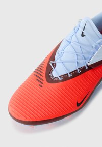 Punane ja oranž jalgpallijalatse koos tekstureeritud pealmise osaga, sinised paelad ja must Nike logo. Omab silmapaistvaid sooni haardeks ja toetuseks.