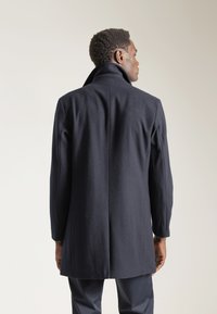 Abrigo de mezcla de lana en color navy con cuello alto, corte recto, uma abertura simple en la parte posterior y textura suave. Presenta mangas largas y un ajuste entallado.