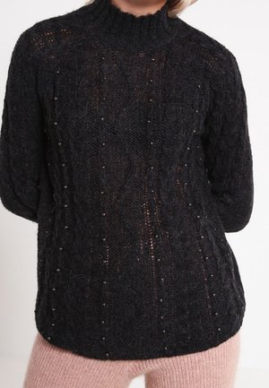 Pull noir en maille avec un col montant, présentant un motif en relief de cables et des perles décoratives le long des lignes verticales.