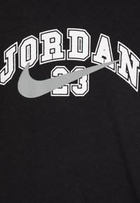 Črna bombažna majica s belimi blok črkami, ki tvorijo napis "JORDAN 23", z sivim Nike swoosh logotipom v središču.