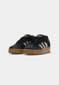 Black suede sneakers with three white stripes, rubber gum sole, and padded collar for comfort. Features a logo on the tongue and side.