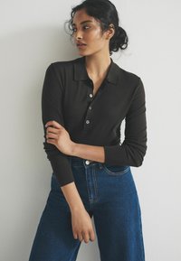 Czarna polo koszula z długim rękawem, z kołnierzykiem i zapięciem na guziki, noszona z niebieskimi dżinsami o wysokim stanie w jasnym odcieniu, z widocznym przeszyciem.