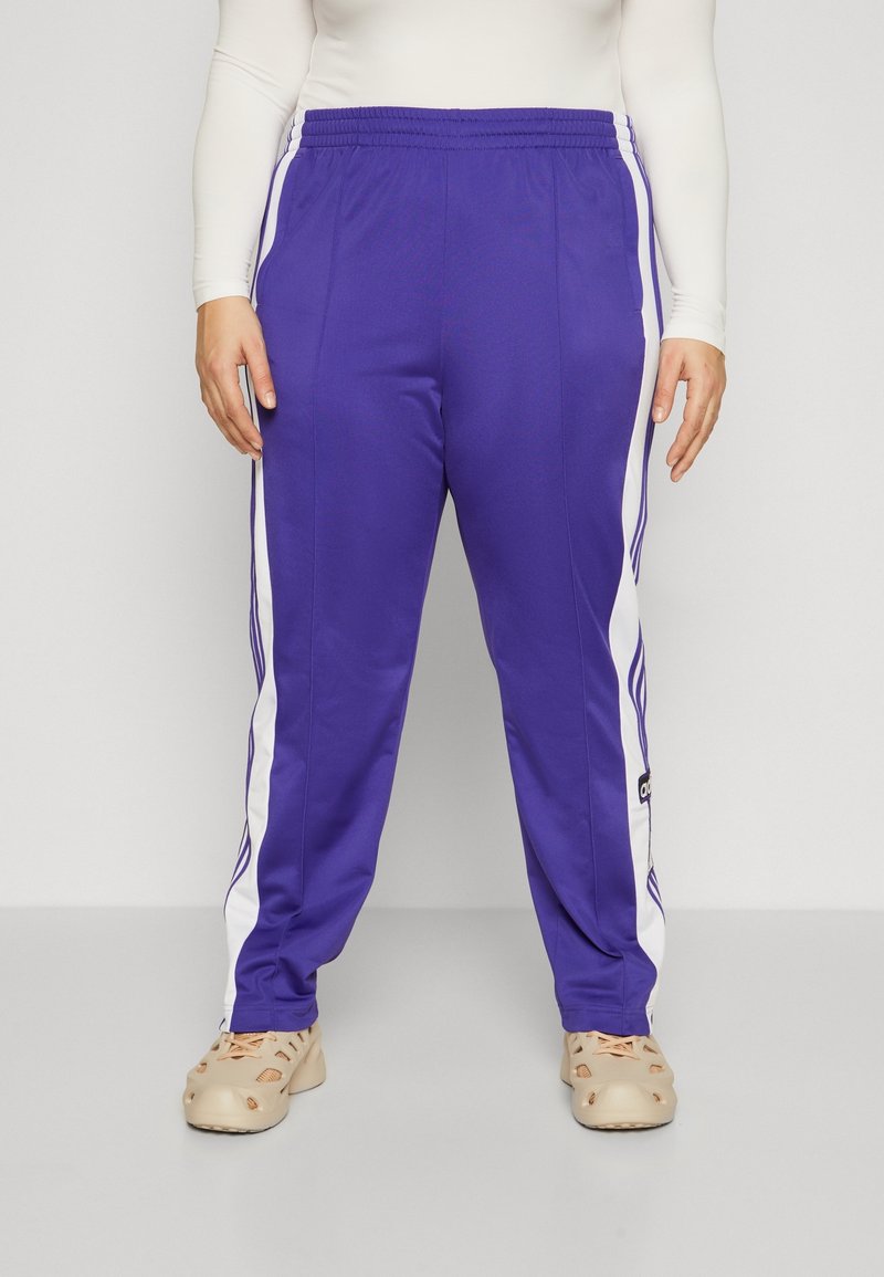 Fialové tepláky s bílými bočními pruhy, elastickým pasem a standardním střihem, vyrobené z hladkého, lehkého materiálu.