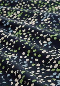 Tessuto di cotone con uno sfondo blu navy e macchie astratte sparse in verde, azzurro e bianco, che presenta una texture liscia.
