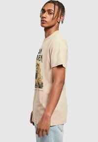 Cremefarvet bomulds t-shirt med et sort grafisk print på fronten, korte ærmer og en afslappet pasform. Ingen synligt logo eller branding.