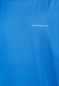 Blå idrottströja av texturerat tyg med rundad halsringning. Har en liten vit "ENDURANCE"-logotyp nära kragen.