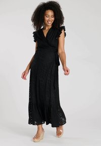 Schwarzes Wickelkleid mit Rüschensäumen, das ein strukturiertes Wellenmuster aufweist. Langes, fließendes Design mit einem ausgestellten Saum und durchsichtigen Akzenten.