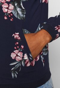 Blommig långärmad topp i marinblått med rosa och gröna mönster, med en sidficka och ribbade ärmslut för textur och detalj.