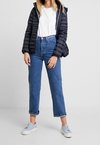 Doudoune noire, t-shirt blanc, jeans bleus taille haute, poignets retroussés et baskets bleu clair. Textures lisses et design décontracté.