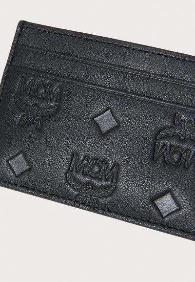 Svart lærhåndholdt kortholder med preget MCM-logo, diamantformer og teksturert overflate. Flere kortlommer med kontrasterende søm.