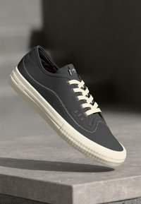 Sorte sneakers med kremfargede snørebånd og gummisåle. Glatt materiale, rund tå, side detaljer, lett design. Enkel, moderne form.