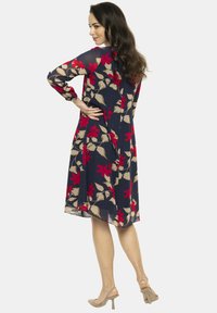 Kwiecista sukienka z czerwonymi i beżowymi wzorami na granatowym tle, z długimi rękawami i rozszerzanym dołem, wykonana z lekkiego materiału.