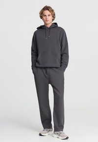 Ciemnoszary hoodie z troczkami i kieszenią na przodzie, dopasowane do niego dresy. Miękka tkanina, luźny krój, noszony z jasnymi sneakersami.