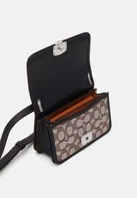 Svart läderhandväska med ett mönstrat framstycke. Har en silverklämma, tanfärgad inredning och justerbar axelrem. Klamshell-design.